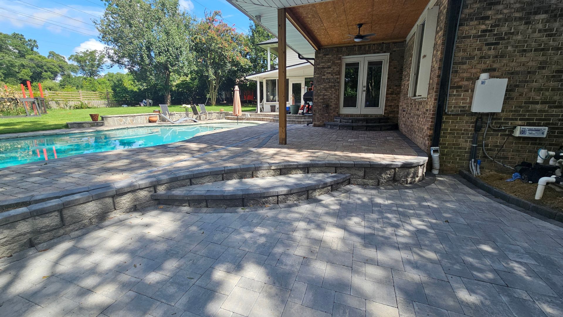 Brick house with stone patio, pool, and shaded seating area