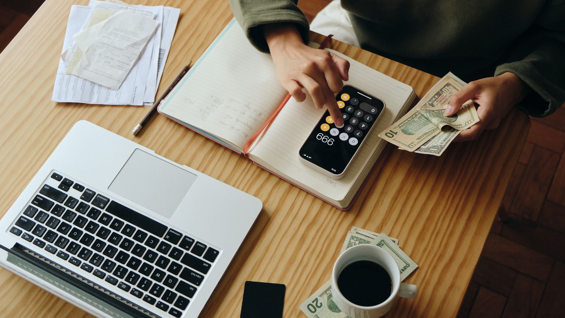 Person calculating finances with laptop, calculator, and money on desk