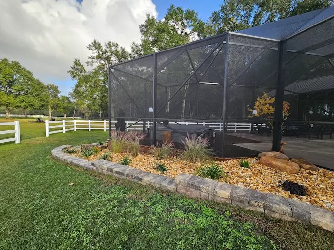 Large mesh enclosure with landscaped garden on grassy property with white fence